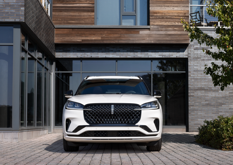 A white 2025 Lincoln Aviator® SUV is shown parked outside a modern building with gray brick and wood accents. | Holmes Tuttle Lincoln in Tucson AZ