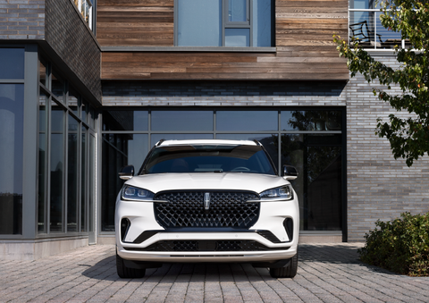 A white 2025 Lincoln Aviator® SUV is shown parked outside a modern building with gray brick and wood accents. | Holmes Tuttle Lincoln in Tucson AZ
