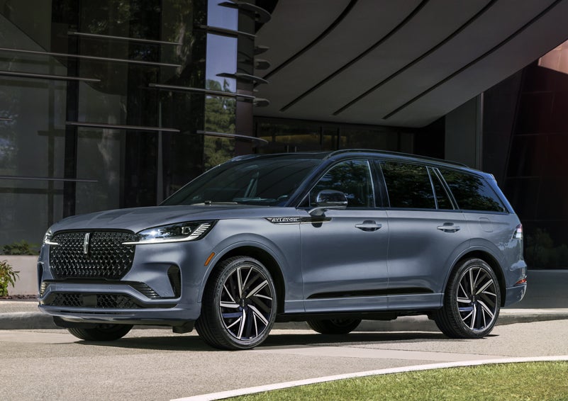 A gray 2025 Lincoln Aviator® SUV is parked outside a modern building showcasing the driver’s side of the vehicle. | Holmes Tuttle Lincoln in Tucson AZ