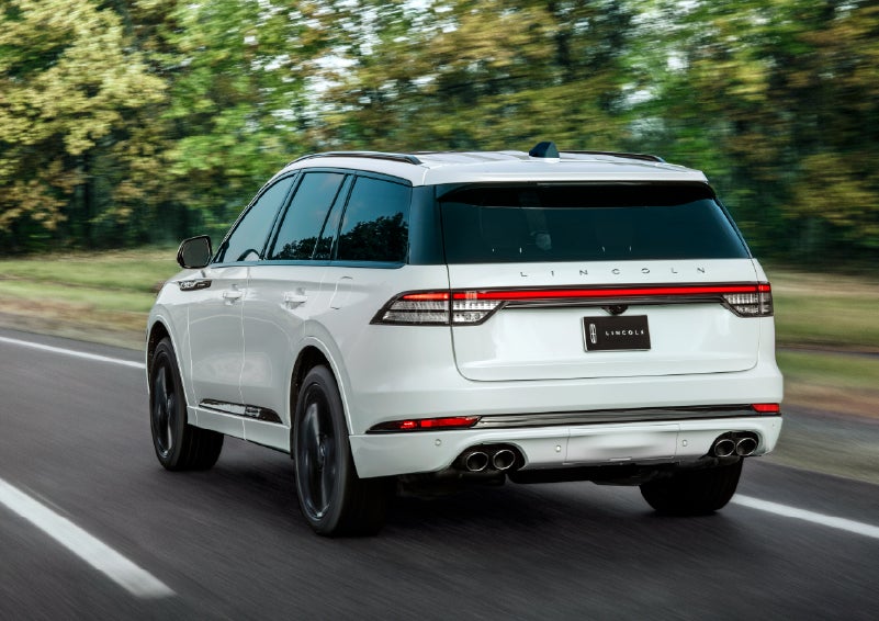 A white 2026 Lincoln Aviator® SUV is being driven away down a road lined with colorful trees. | Holmes Tuttle Lincoln in Tucson AZ