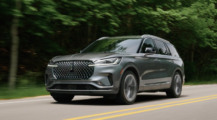 A 2027 Lincoln Aviator® SUV is being driven down a road lined with trees. | Holmes Tuttle Lincoln in Tucson AZ