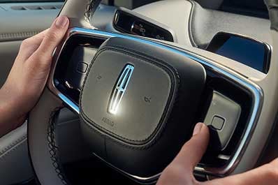 A woman holding the steering wheel inside a Lincoln vehicle.E#